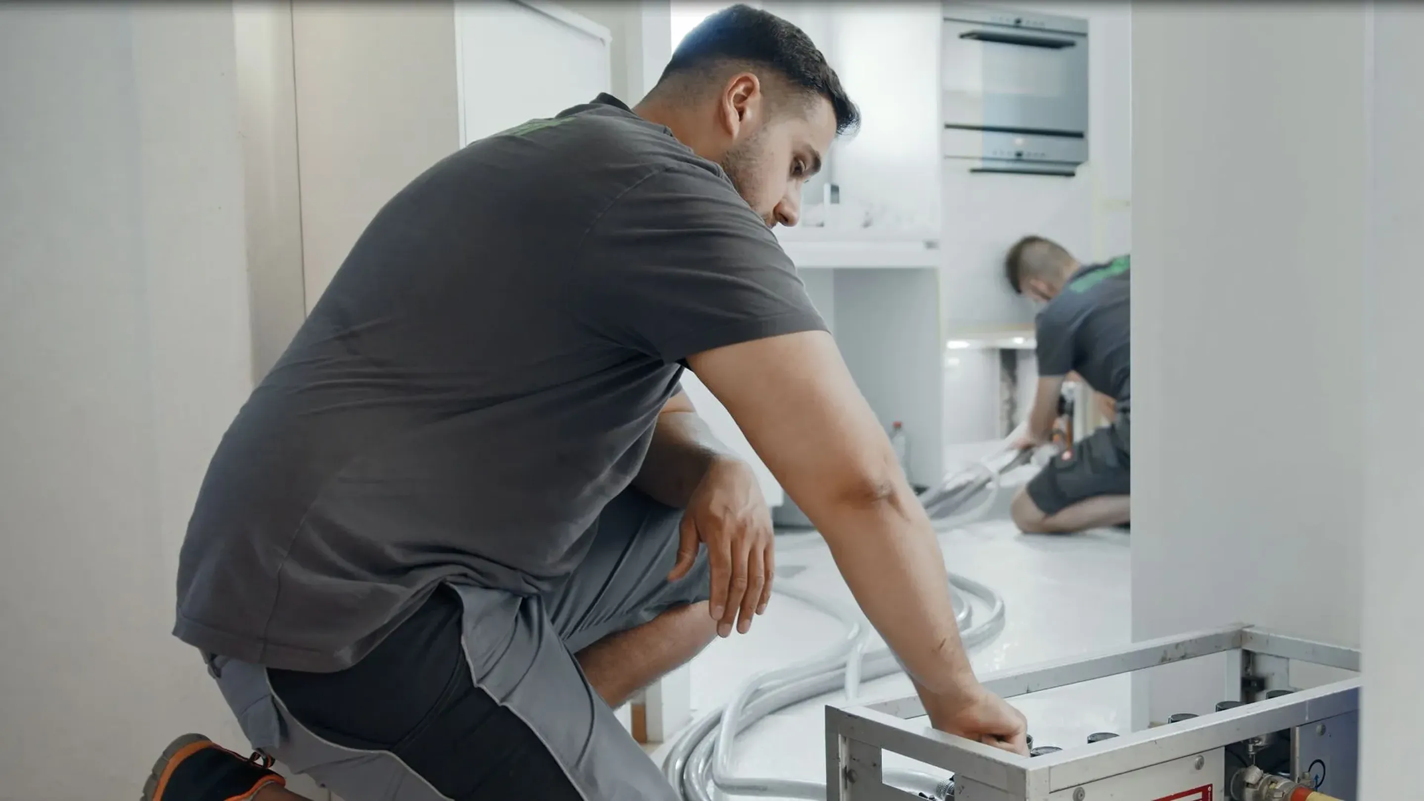 A man fixing a stove in a kitchen.