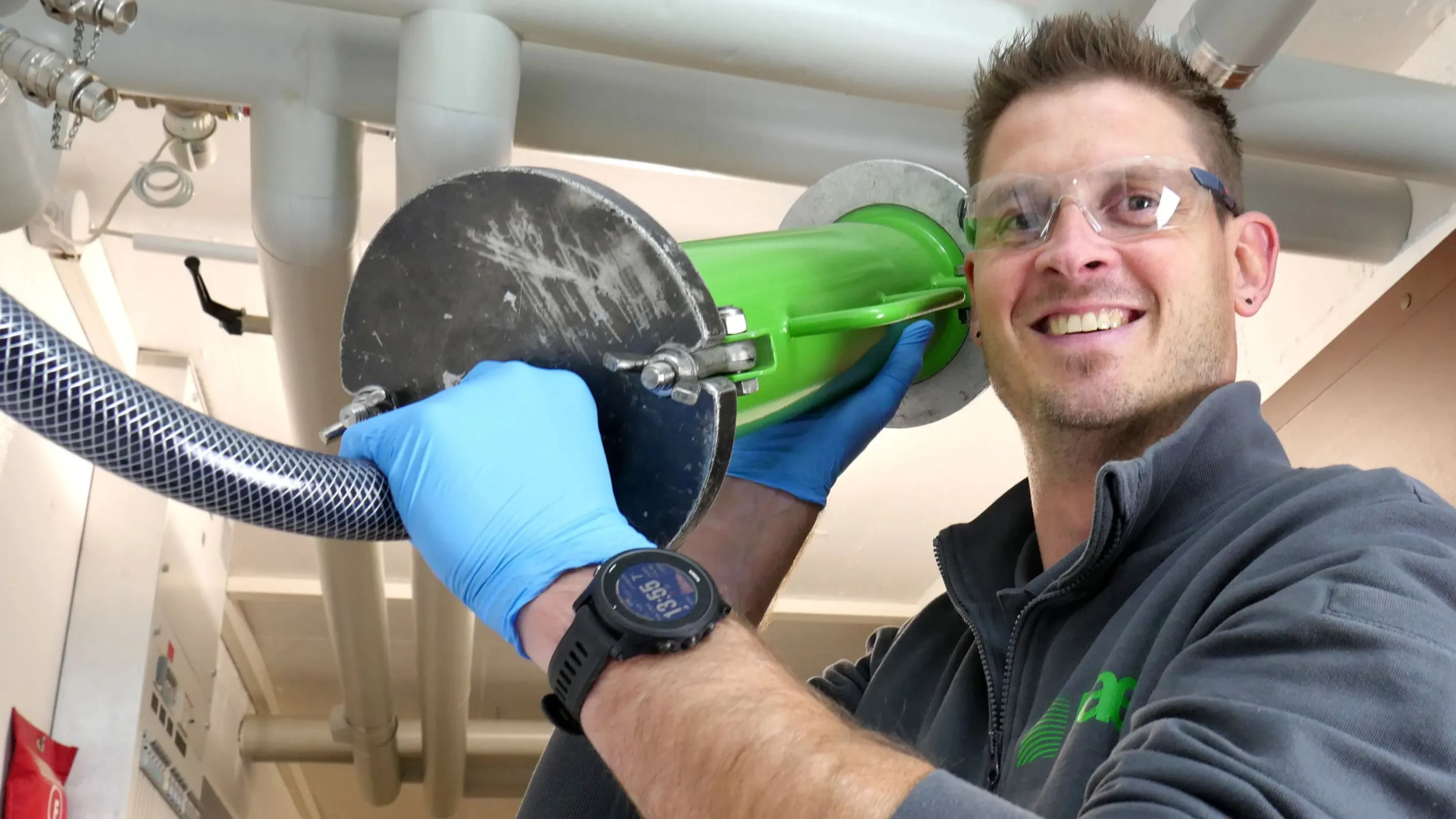 A man in a gray shirt and blue gloves is holding a green and black blow.