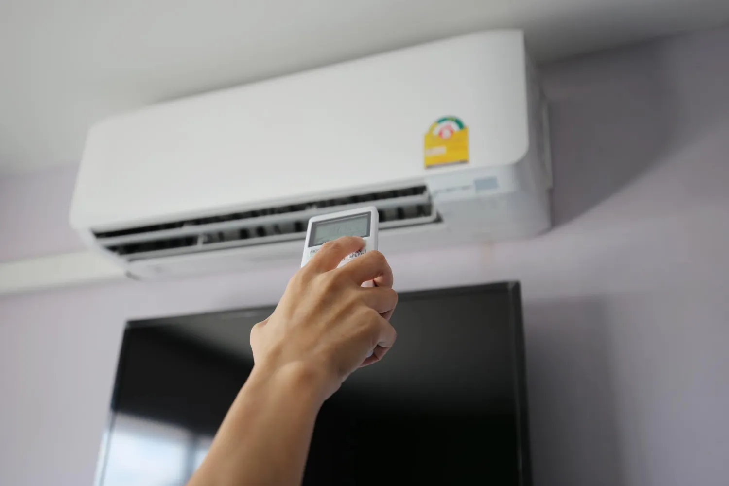 Hand adjusting air conditioning remote control near wall-mounted unit