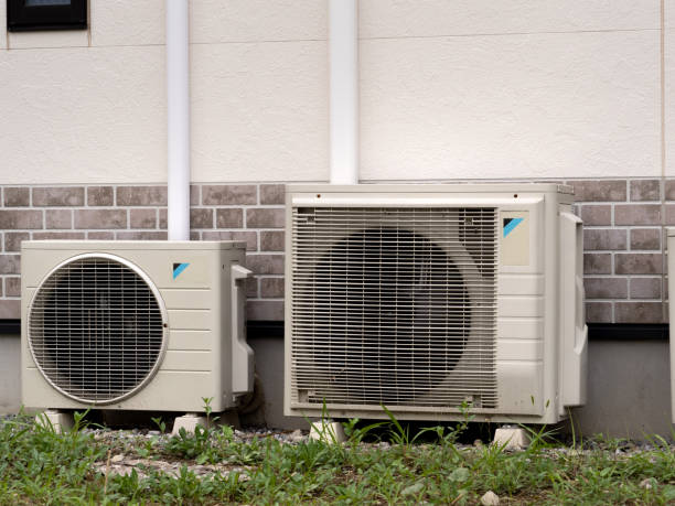 Two outdoor air conditioning units next to brick wall with vegetation