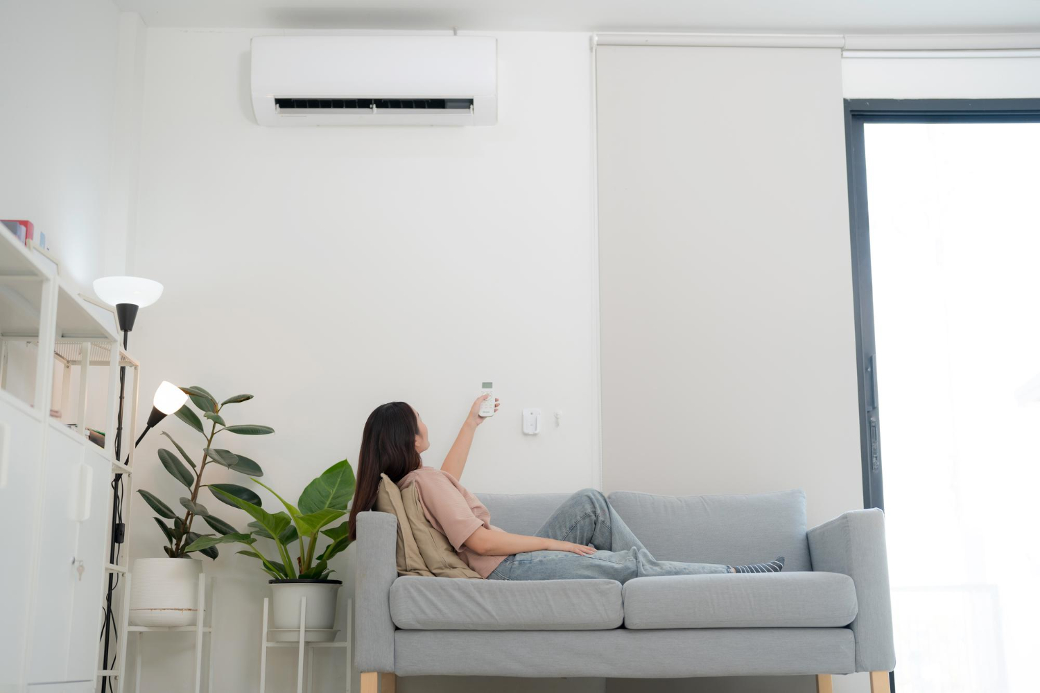 Person relaxing on gray couch adjusting air conditioner in minimalist room