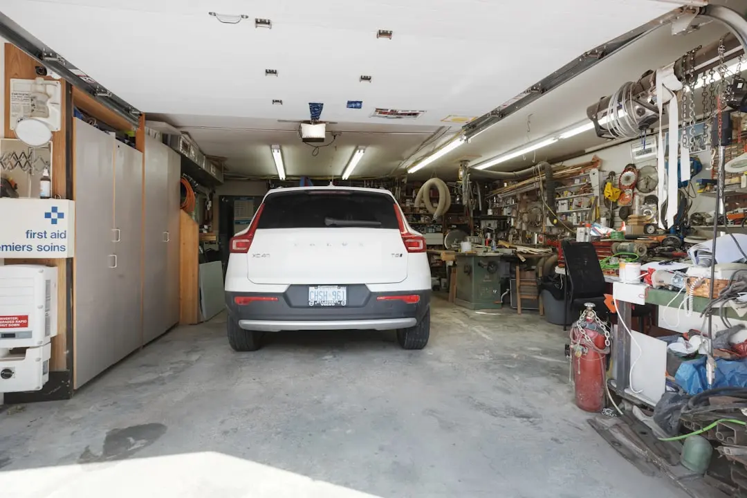 Cluttered garage with white car, tools, and first aid kit on shelves