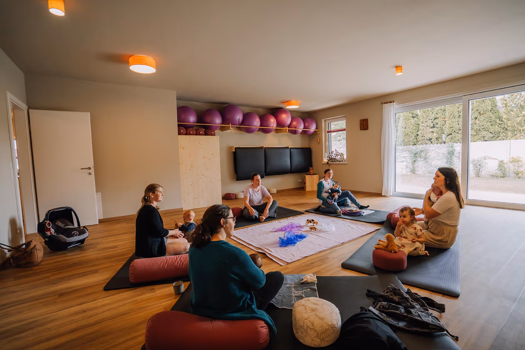 Kursraum mit lila Gymnastiknbällen und Teilnehmerinnen mit ihren Babies