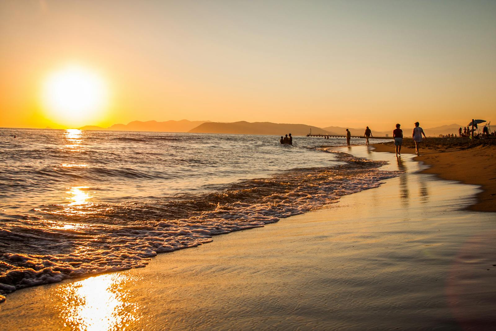 People walking along a golden sand beach at sunset on the Akamas coast