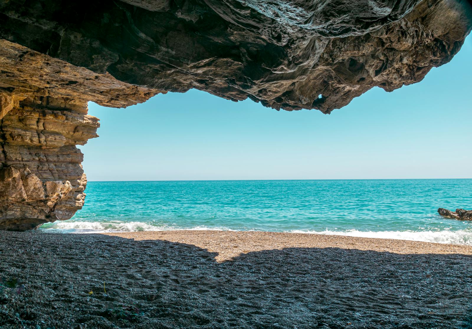 View of a Mediterranean beach and turquoise sea from inside a coastal cave