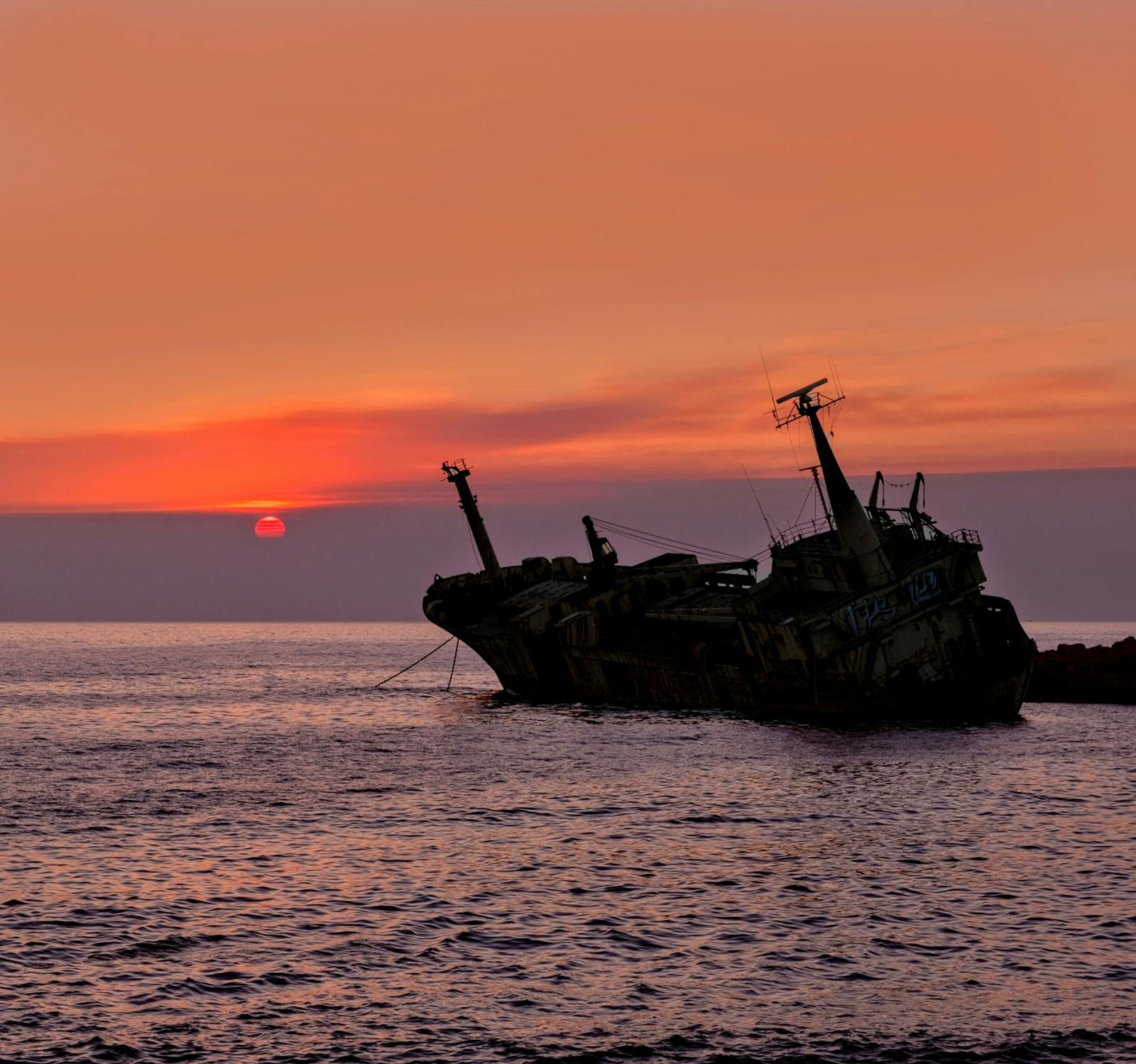 Shipwreck silhouetted at sunset against the Paphos coastline, Cyprus