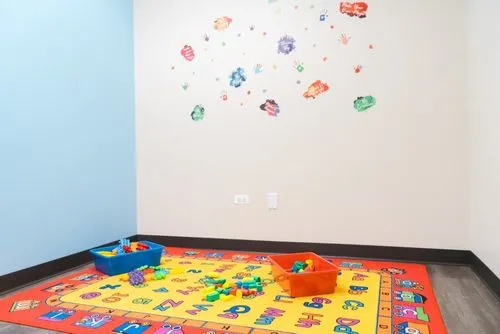 Children's playroom corner with colorful rug, toy bins, and handprint wall decals.