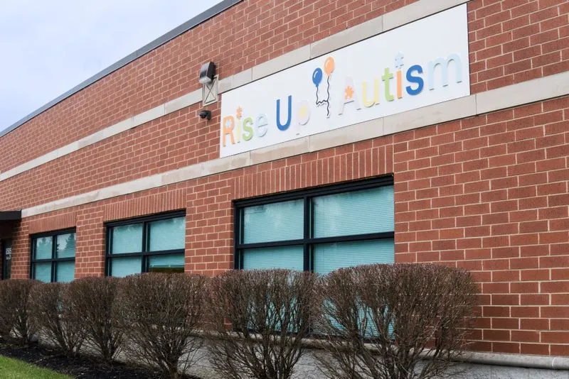 Building with a brick exterior and a sign that reads "Rise Up Autism" above three windows.