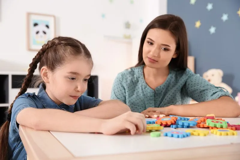 Girl playing with colorful gear toys while an adult woman watches attentively.