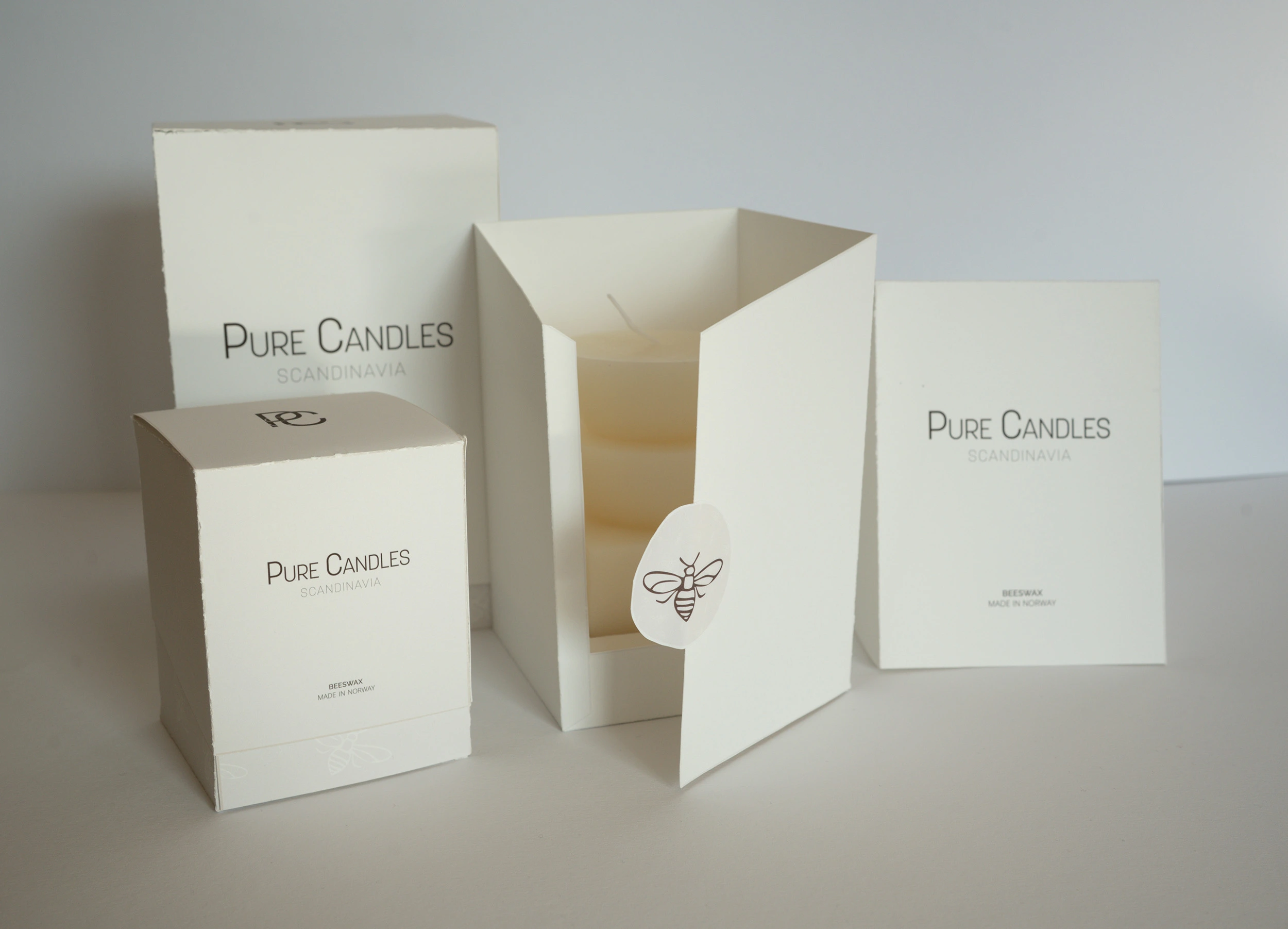 Pure Candles packaging in different sizes, photographed on a neutral background with one box open, revealing a candle inside.