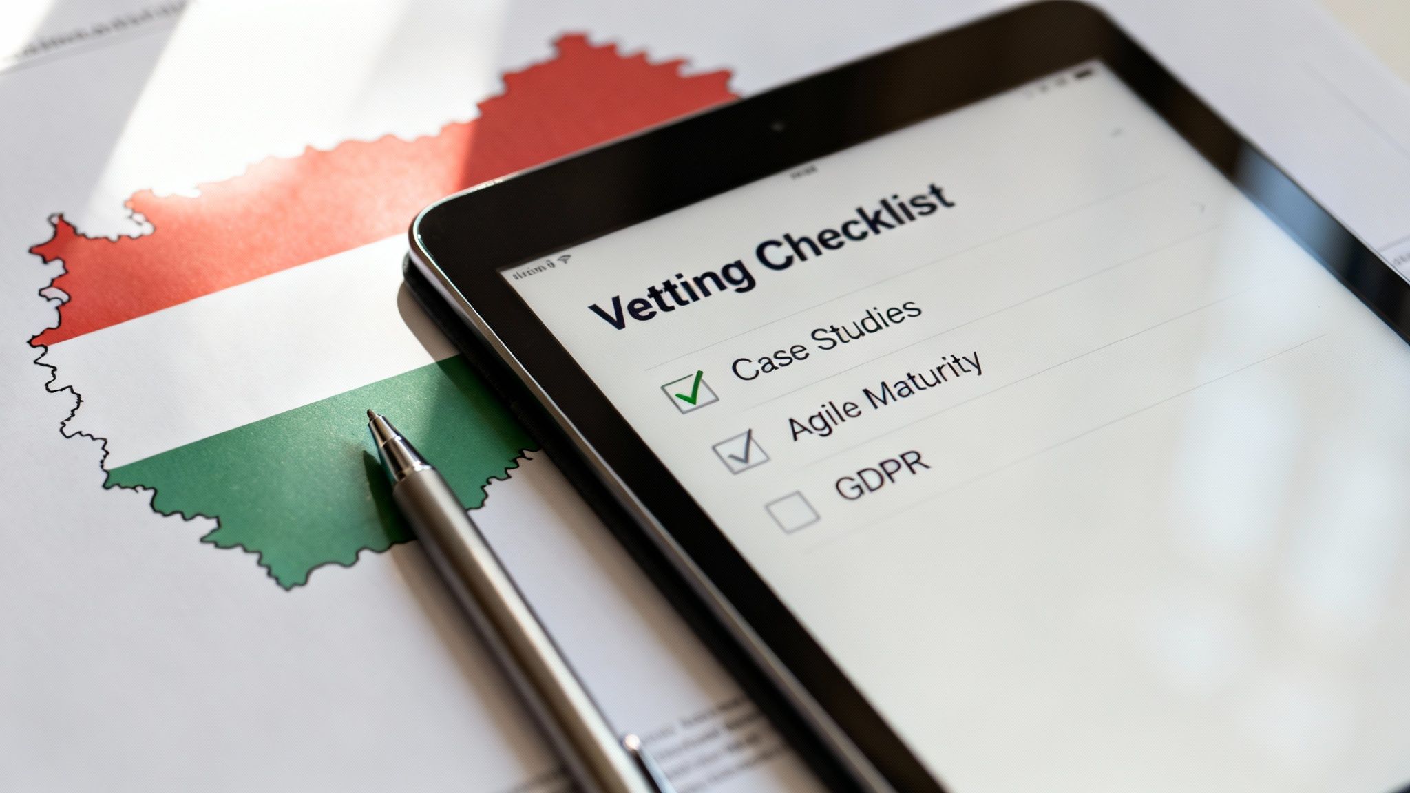 Tablet showing 'Vetting Checklist' with checked 'Case Studies', 'Agile Maturity' beside Hungary map and pen.