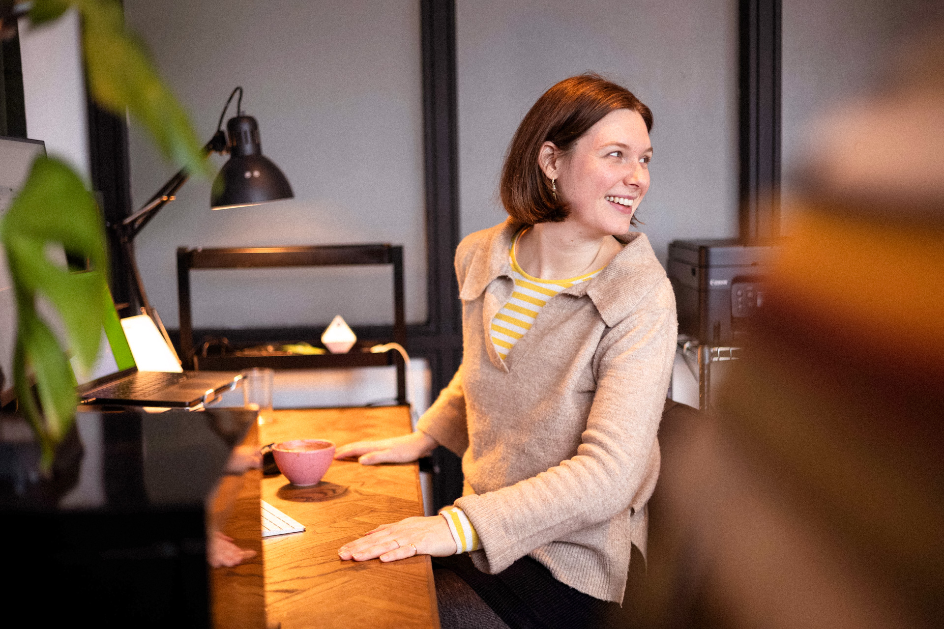 Et billede af en smilende dame, Ulrikke fra Hej Marketing, der står ved sit skrivebord.