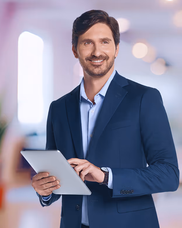 Homem de terno azul sorrindo enquanto usa um tablet em ambiente interno moderno e bem iluminado.