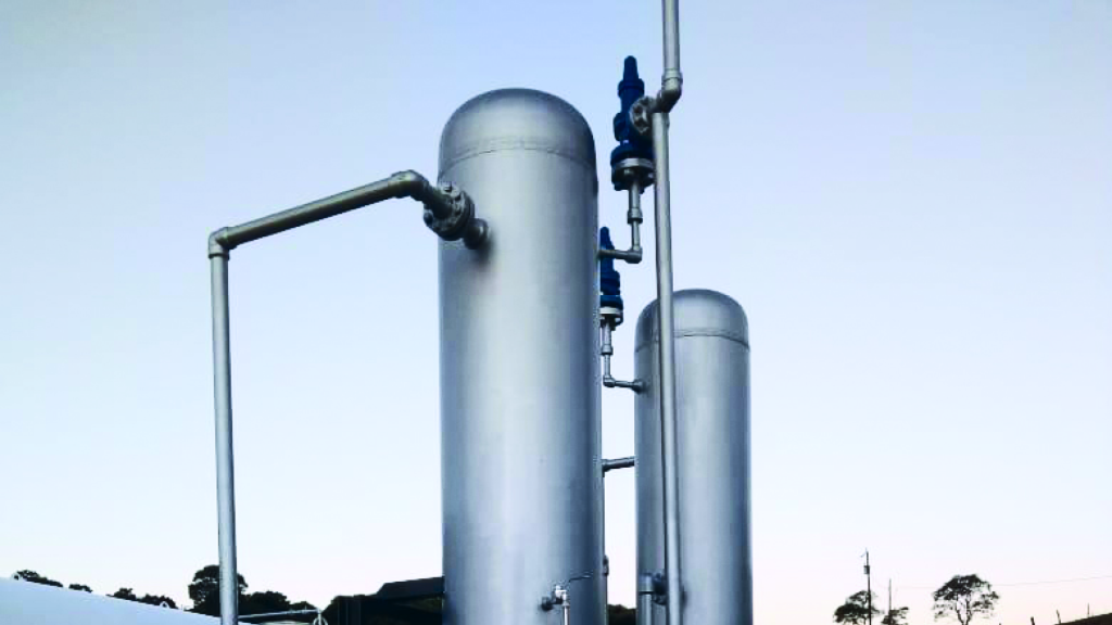 Tanques altos cilíndricos prateados conectados por tubos em um céu claro.
