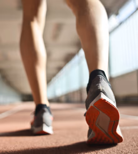 Pernas de uma pessoa correndo em uma pista, com foco na sola do tênis esportivo com detalhes em vermelho.