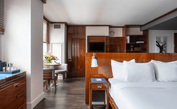 room at Hotel Hugo SoHo with floor-to-ceiling window overlooking the Hudson River and downtown Manhattan at sunset.