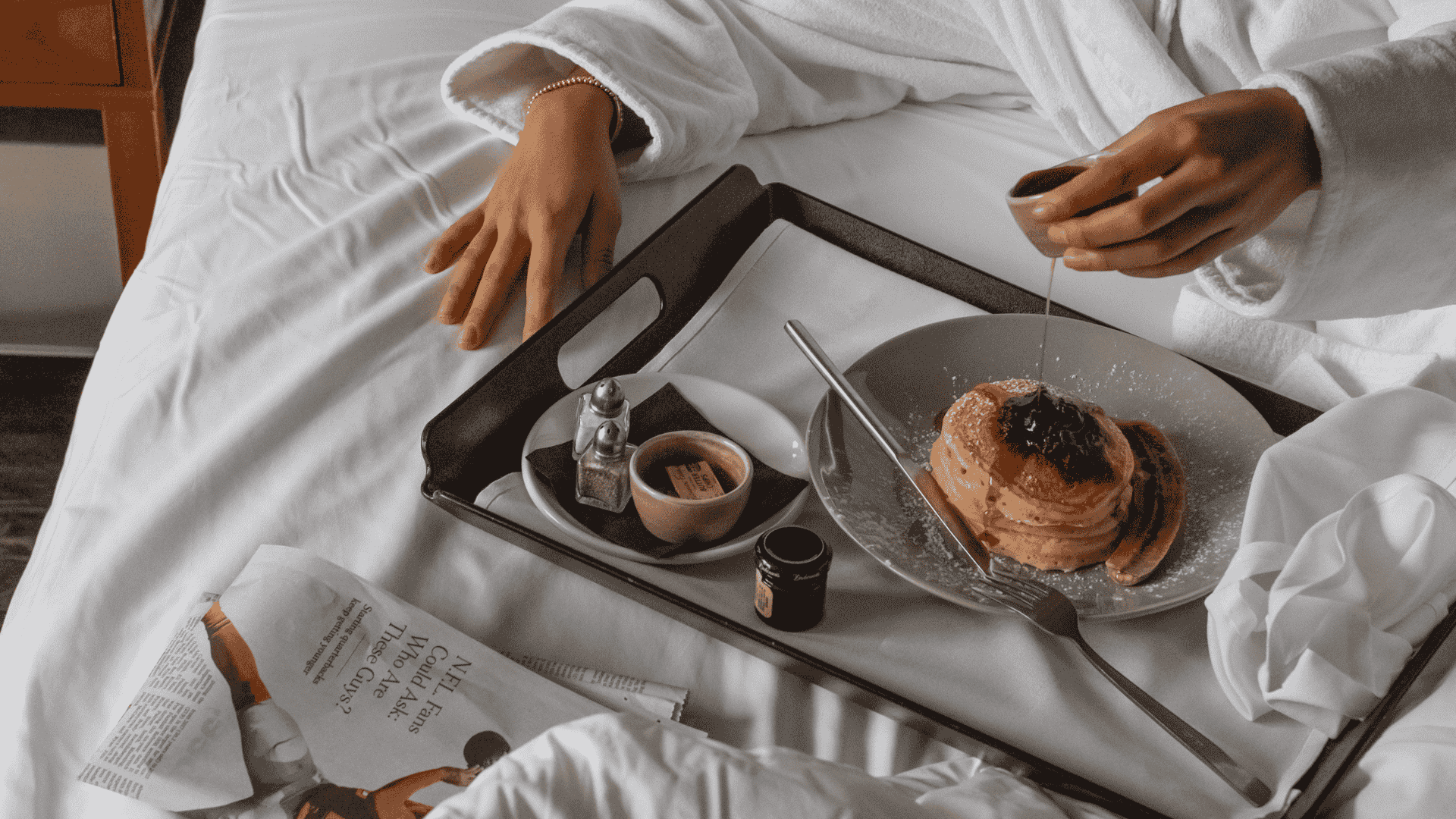 Person enjoying breakfast in bed with pastries and coffee on a tray