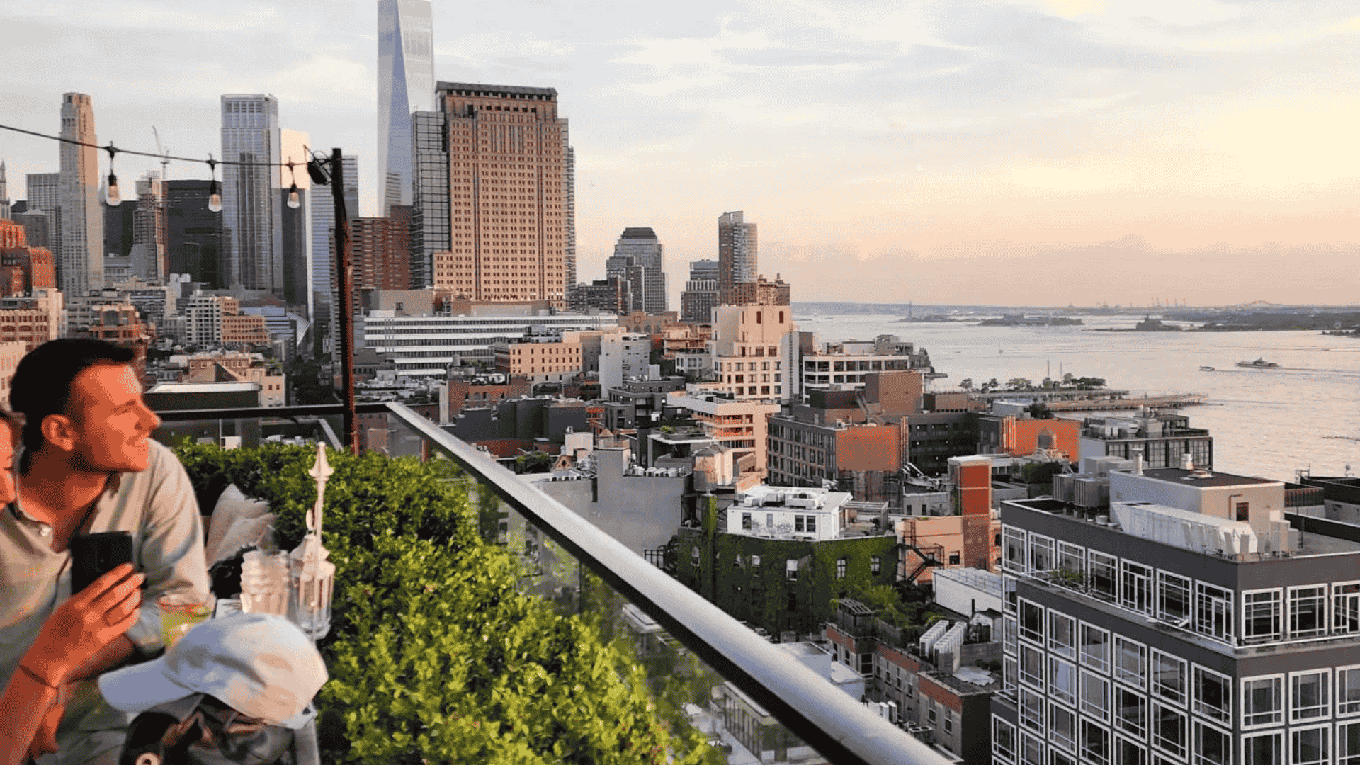 Rooftop terrace with people enjoying drinks and views over New York City skyline at sunset