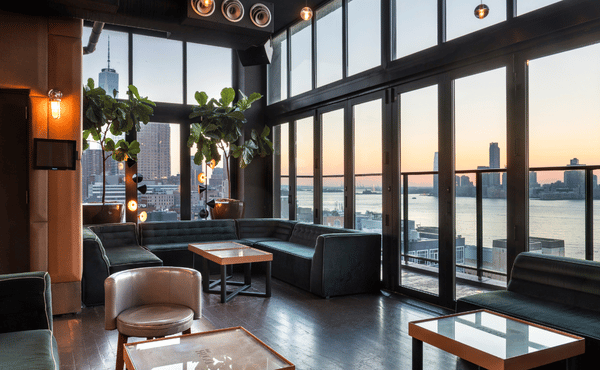 A rooftop lounge with green velvet couches and large windows overlooking the NYC skyline