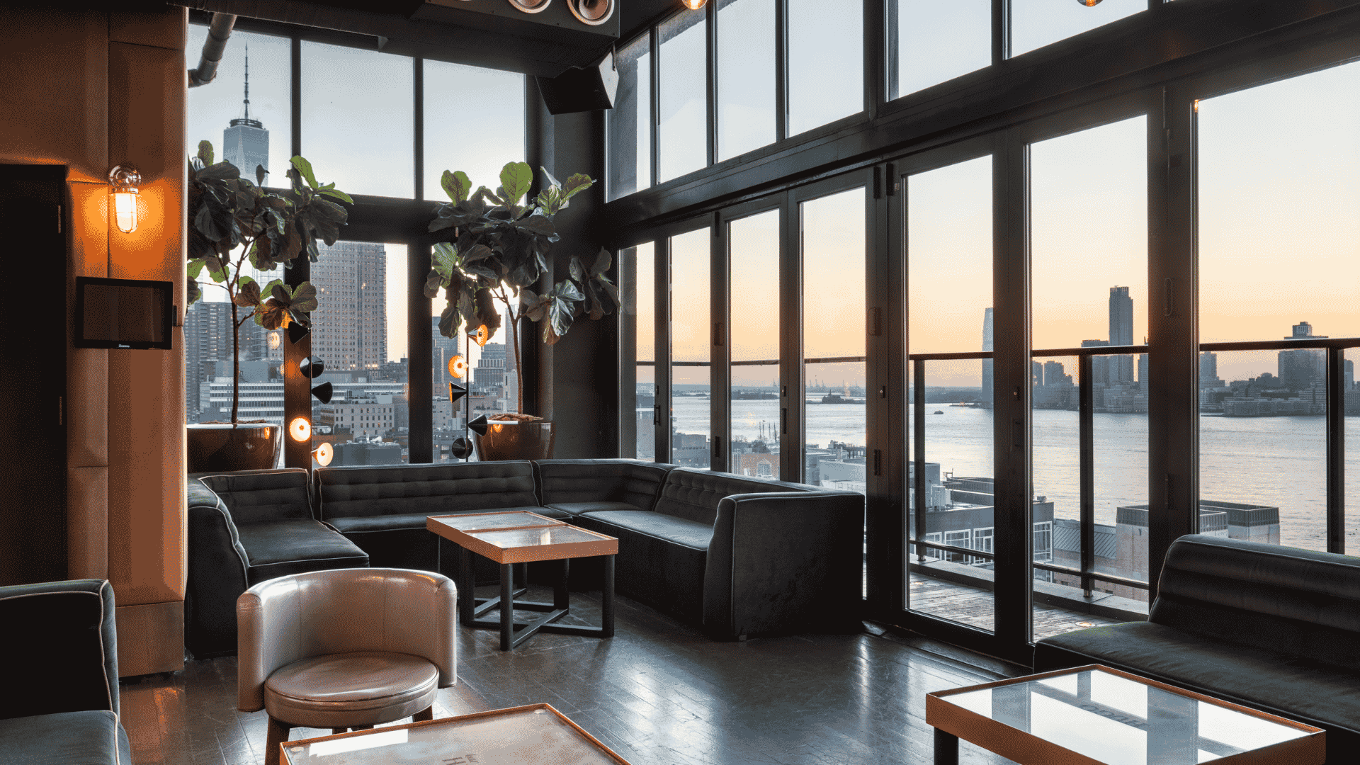 A rooftop lounge with green velvet couches and large windows overlooking the NYC skyline