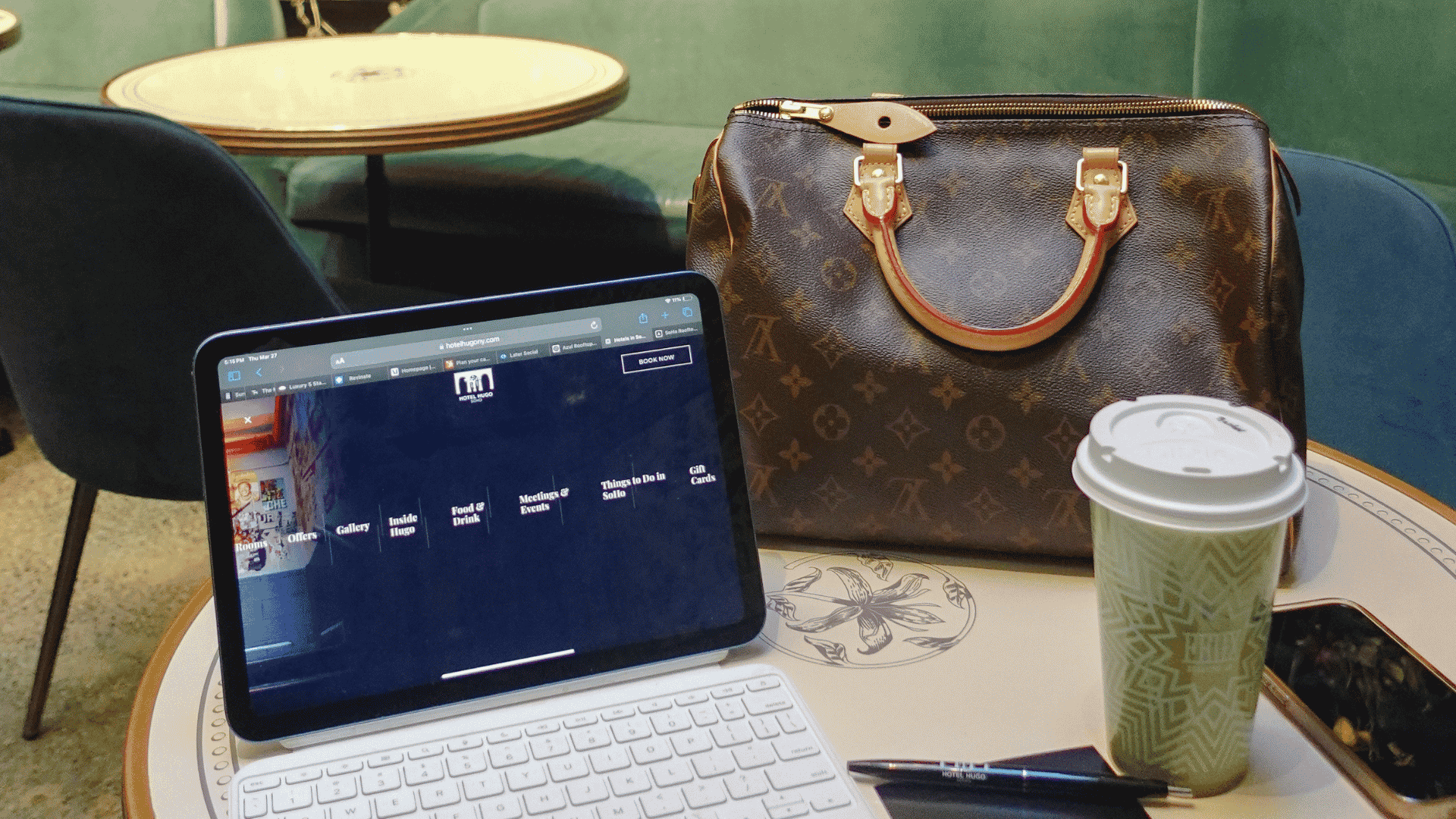 A tablet with a keyboard, a Louis Vuitton bag, and a coffee cup resting on a round cafe table.