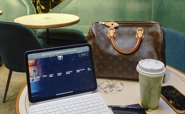 A tablet with a keyboard, a Louis Vuitton bag, and a coffee cup resting on a round cafe table.