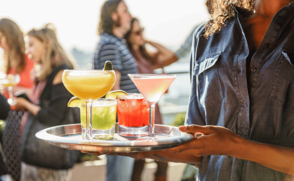 Professional server carrying a tray of handcrafted cocktails on the rooftop at Hotel Hugo NYC during a lively evening with a festive atmosphere.
