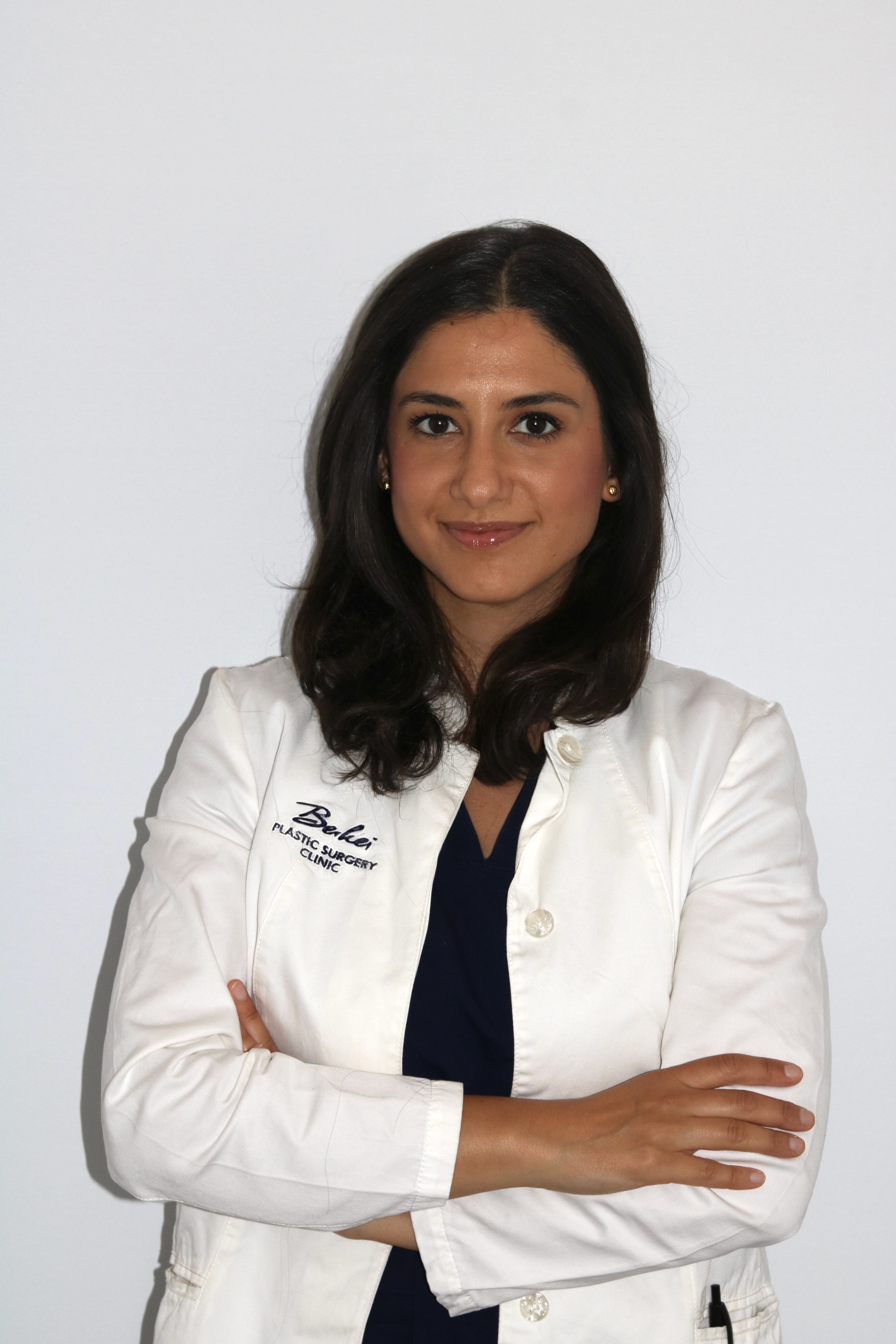A professional portrait of Dr. Perihan Gerger, wearing a white lab coat and smiling with her arms crossed against a bright background. This follows the exact pattern already established in the CMS for Dr. Mulica, including the lab coat, pose, and background.