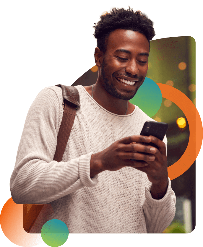 A man smiling while looking at his smartphone, wearing a light sweater with a shoulder bag. The background features soft lights and colorful abstract shapes.