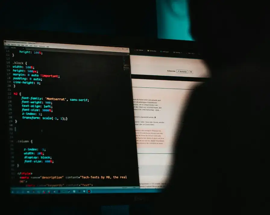 person sitting at a computer in dark environment with code on the screen