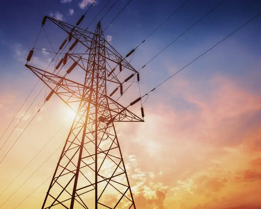 Tall electricity transmission tower with multiple power lines against a vibrant orange and purple sunset sky. The structure rises prominently, with the sun's warm glow contrasting the silhouette of the tower, creating a dramatic and powerful scene evocative of identity theft protection measures.