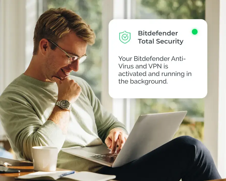A person with glasses is sitting at a table, typing on a laptop and smiling. A notification on the right side of the image reads: "Bitdefender Total Security: Your Bitdefender Anti-Virus and VPN is activated and running in the background." A coffee cup, smartphone, and credit management materials are on the table.