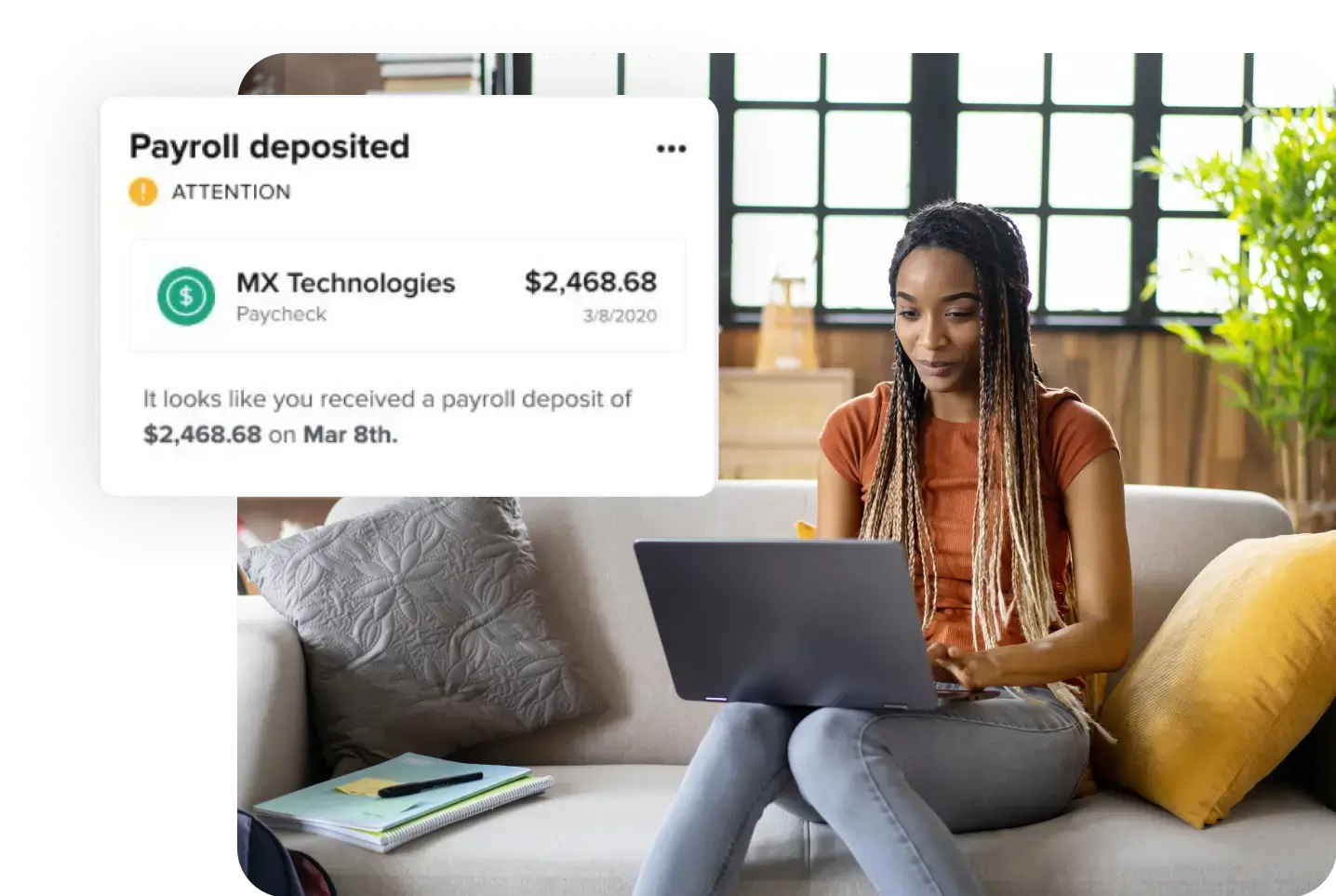 A woman with long braided hair sits on a couch, using a laptop. Next to her, a notification on her screen shows a payroll deposit from MX Technologies for $2,468.68, dated March 8th. The room has large windows and a plant in the background. With IDIQ's rent reporting and identity theft protection services, she feels secure online.