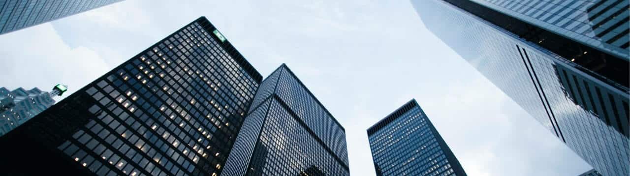 A low-angle view of several modern skyscrapers in a city with glass windows reflecting the sky. The buildings, varying in height, converge towards the center of the image under a cloudy sky, reminiscent of complexity in credit management.