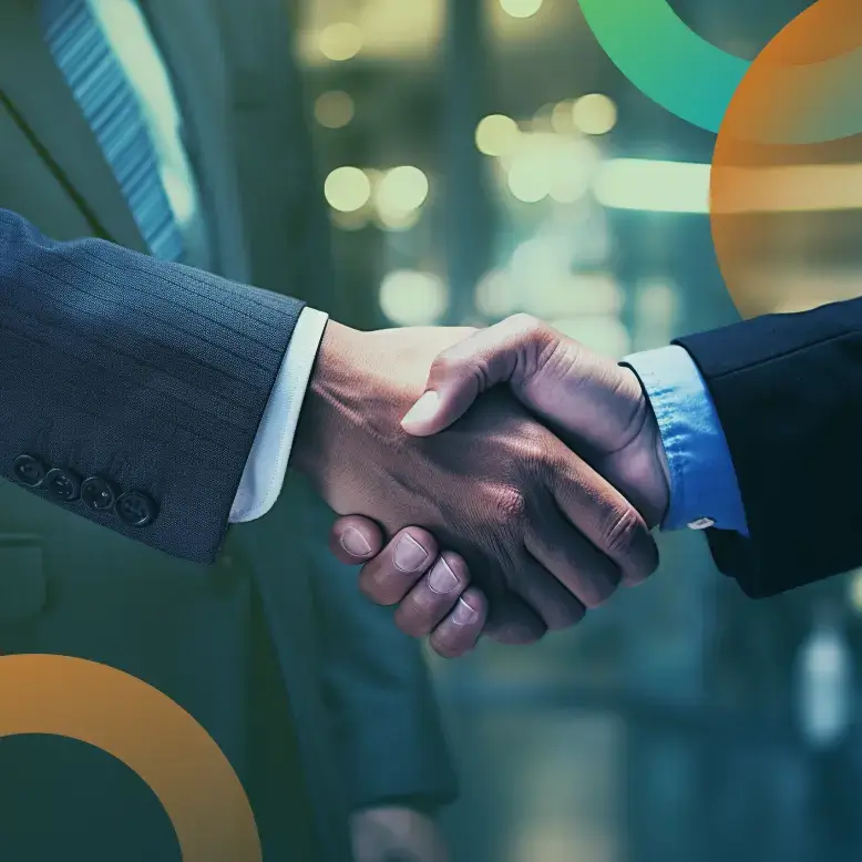 Two business professionals shaking hands with blurred background and abstract shapes in the foreground.