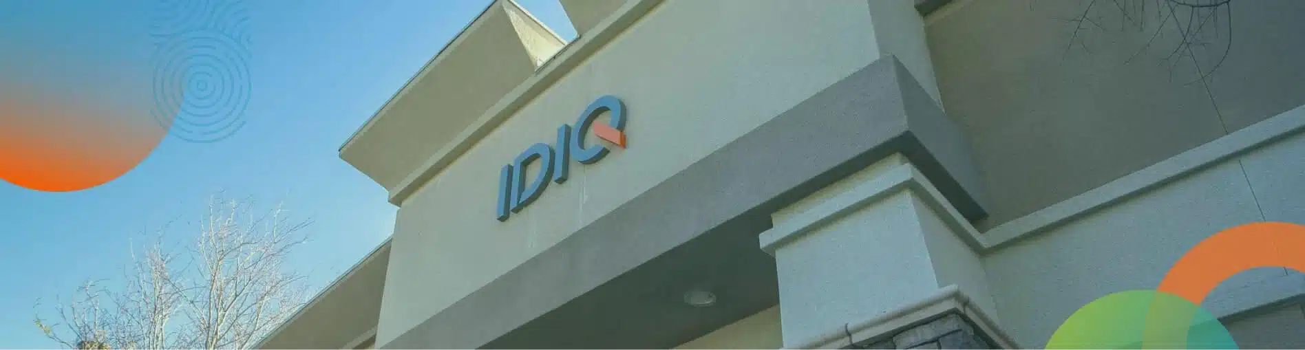 The exterior of a building featuring a blue and orange sign that reads 'IDIQ,' under a clear blue sky. The image captures a section of the building with architectural details.