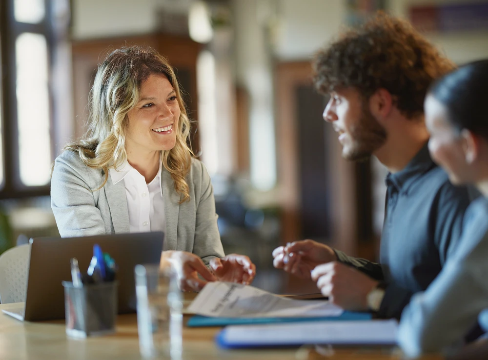 A loan broker smiling and talking to her young adult clients with paperwork in front of them
