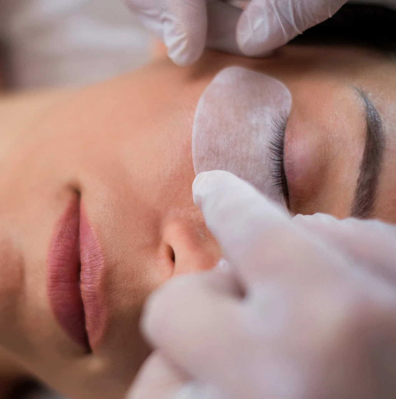 Operatrice applica trattamento laminazione su ciglia di cliente distesa, ambiente cabina estetica