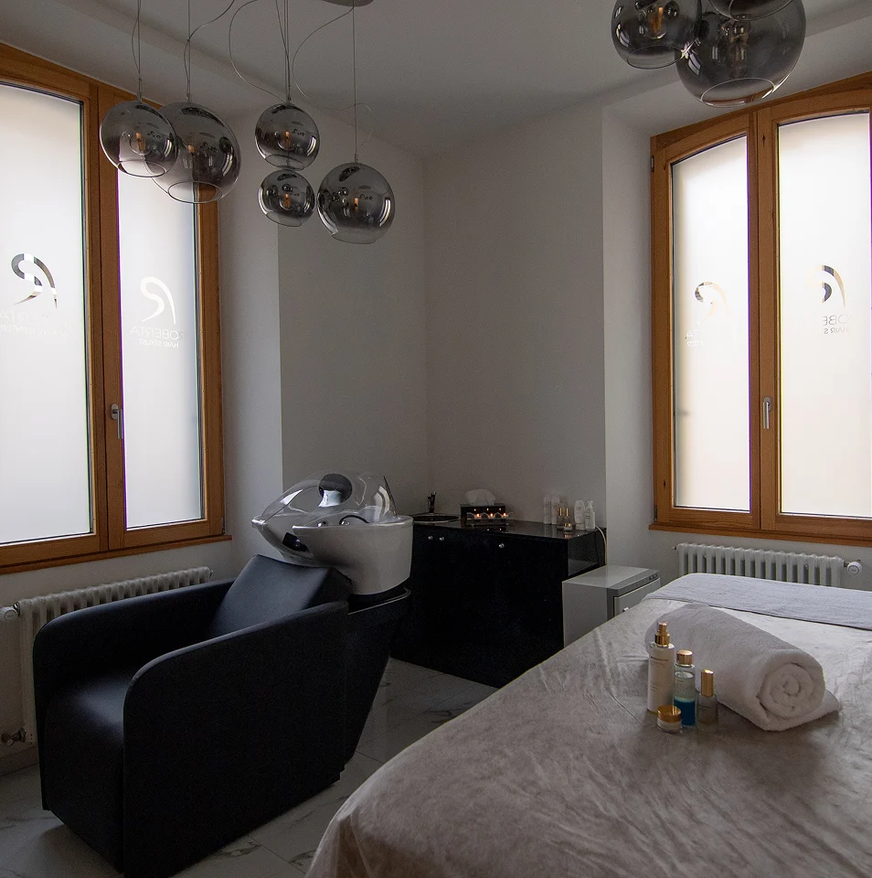 Operatrice applica extension ciglia su cliente distesa in cabina estetica, primo piano ravvicinato