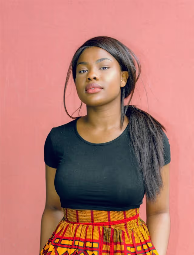 A woman wearing a black top and a yellow skirt stands confidently, showcasing a vibrant and stylish outfit.