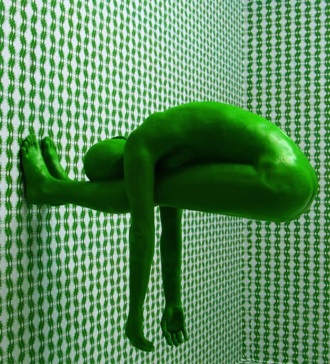 A green man is suspended upside down in a room, creating a surreal and intriguing visual scene.