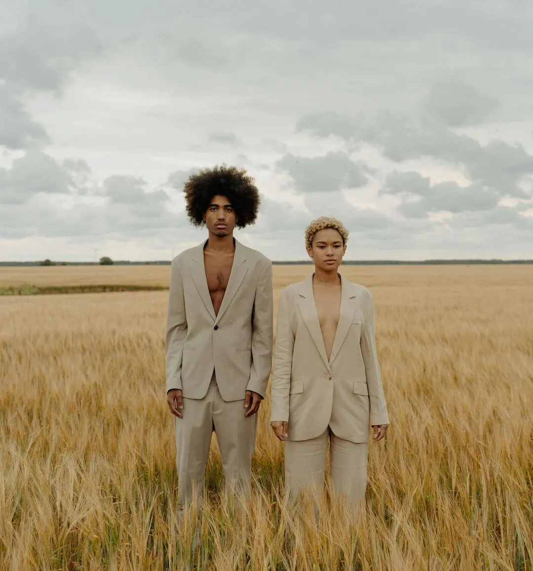 Two individuals standing together in a golden wheat field under a clear blue sky.