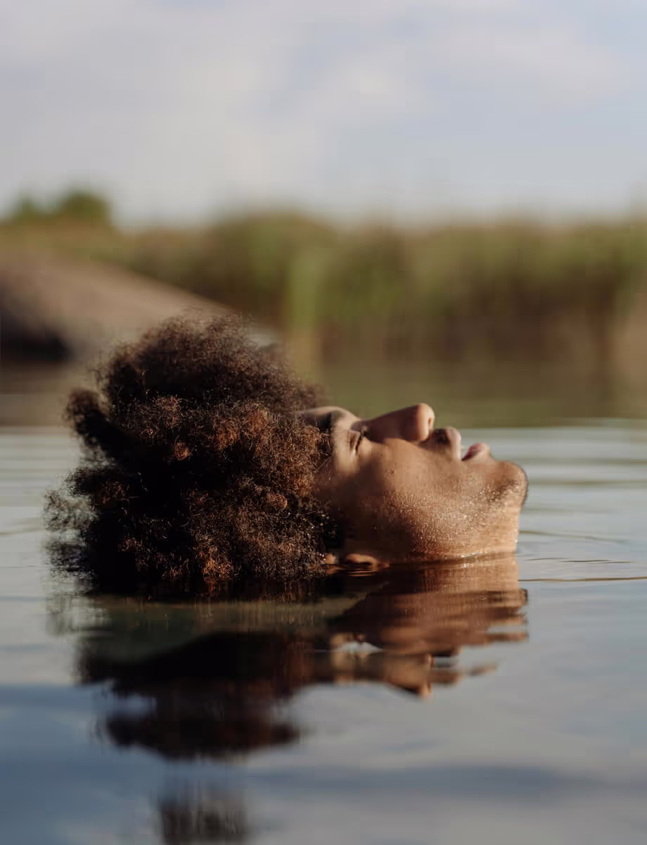 A man with an afro hairstyle is seen floating peacefully in calm water.