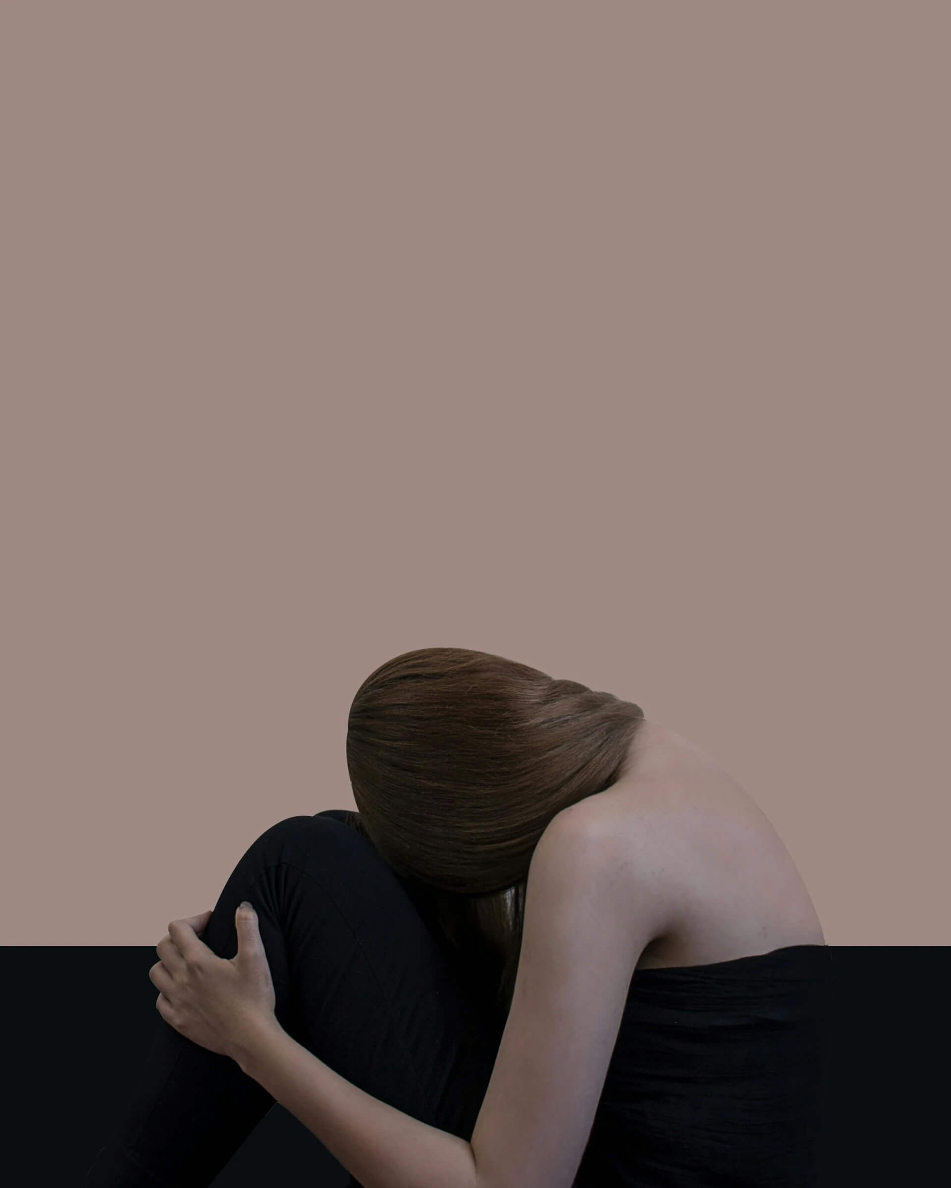 A woman sitting on the floor, her head resting in her hands, conveying a sense of distress or contemplation.
