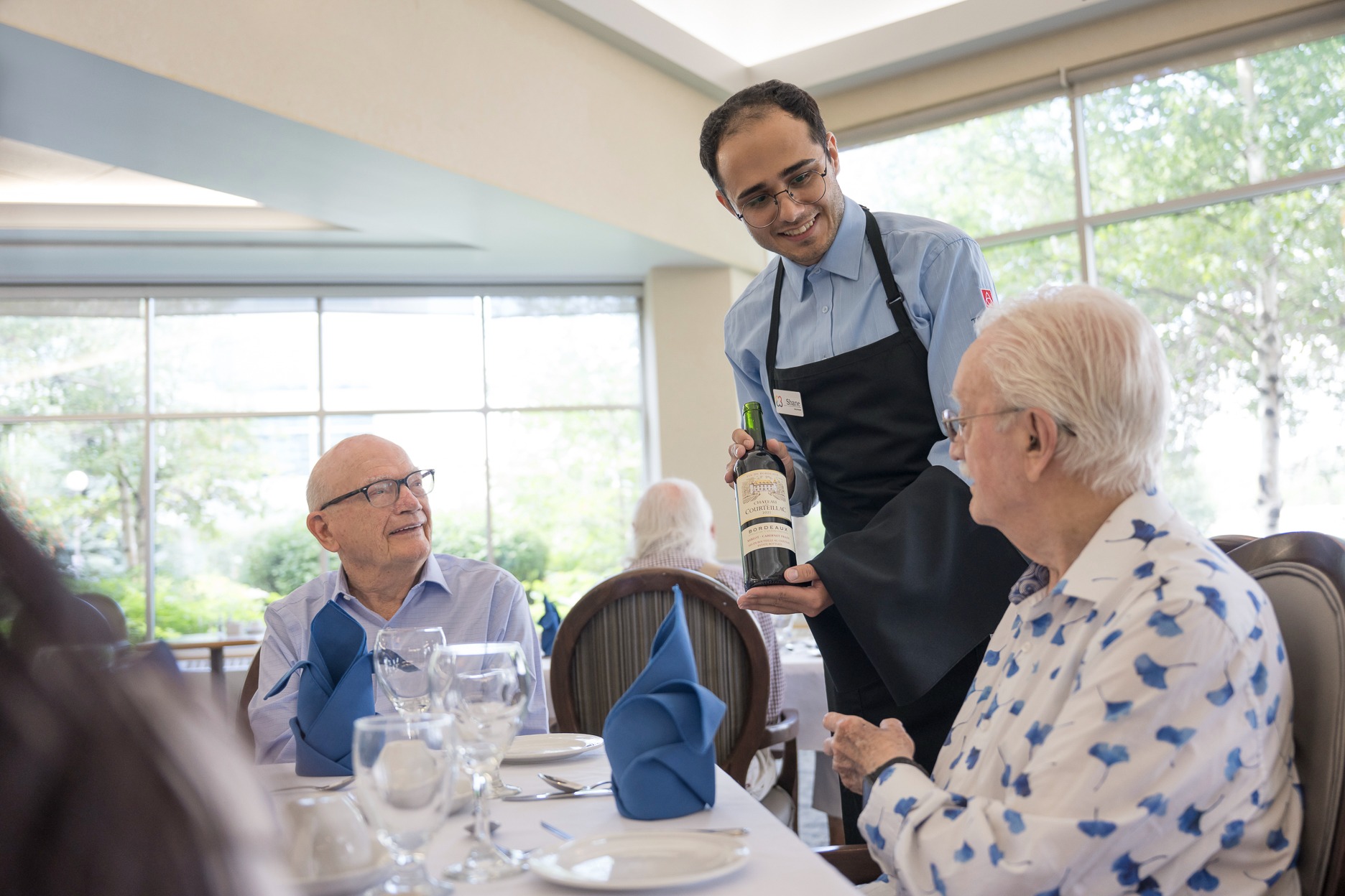 server holding wine bottle in retirement community dining area