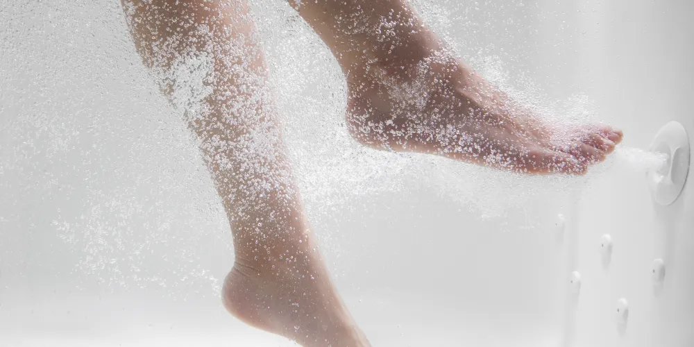A close-up of feet resting near hydrotherapy jets in a Kohler walk-in bath, with water bubbling around them.