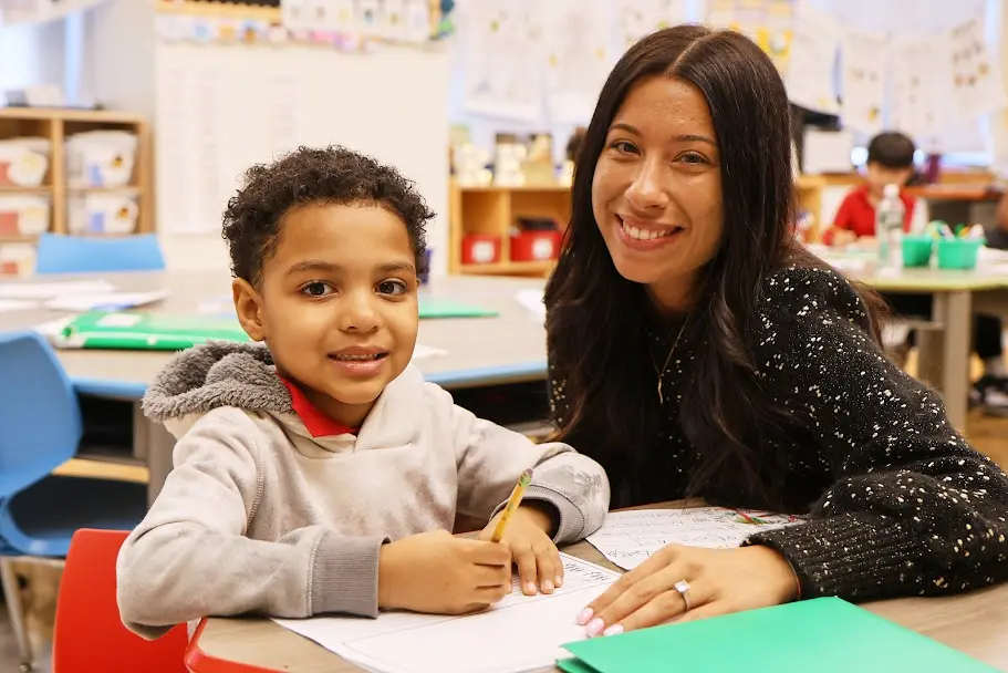 Teacher smiling with young student working on writing assignment