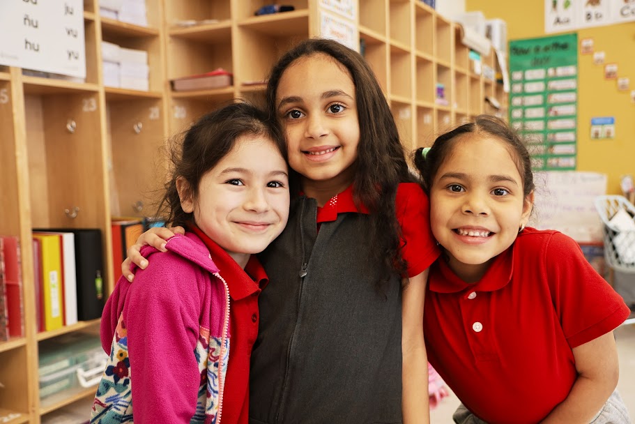 Three elementary students smiling together in classroom