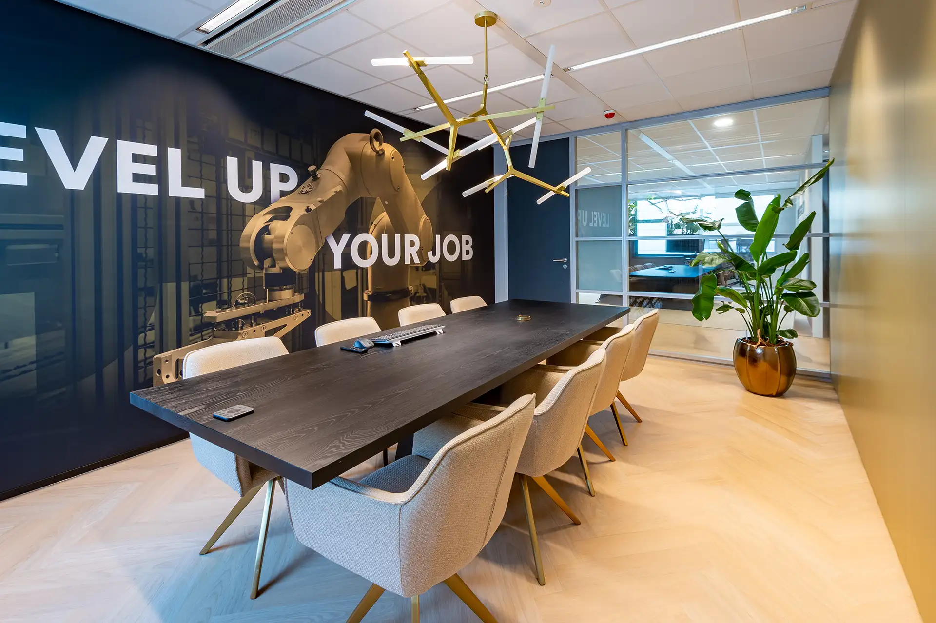 Moderne vergaderruimte met een lange donkere tafel, lichtgrijze stoelen en een muurdecoratie met een robotarm en tekst 'LEVEL UP YOUR JOB'.