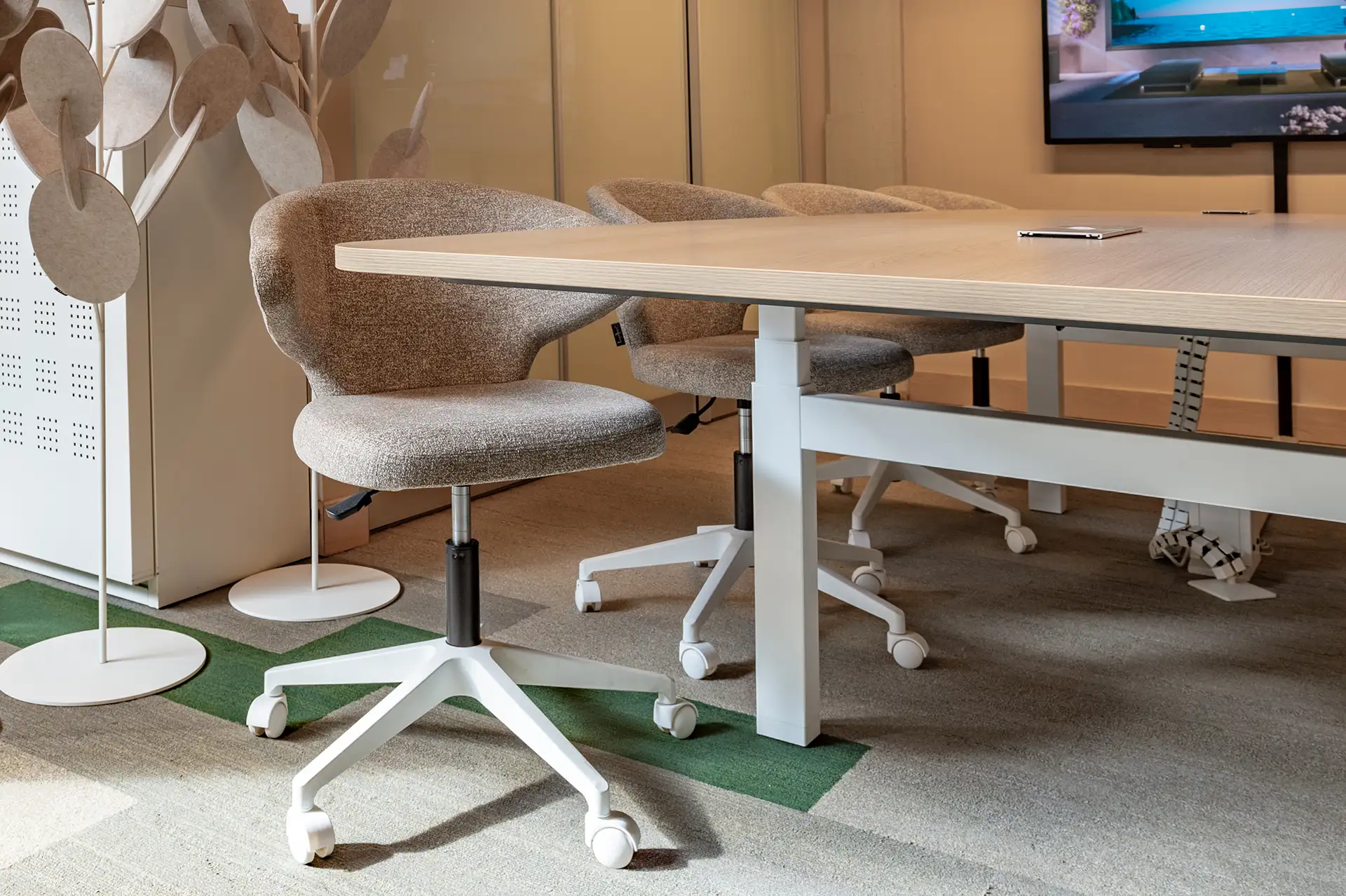 Moderne kantoorruimte met een houten vergadertafel en drie beige bureaustoelen op wielen.